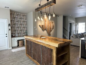 Une cuisine avec un îlot central en bois, une œuvre d’art murale de style rustique et un papier peint à motifs.
