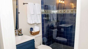 A bathroom with a white toilet, blue cabinets, a glass shower enclosure, and a tiled backsplash. - St. Augustine Apartment: Walk to Historic Sites! (St. Augustine)