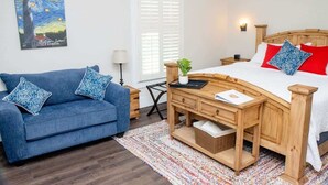 A bedroom with a wooden bed, a blue sofa, a small table, and a painting on the wall. - St. Augustine Apartment: Walk to Historic Sites! (St. Augustine)