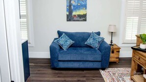 A living room with a blue sofa, patterned pillows, a painting of a lighthouse, and a lamp on a wooden side table. - St. Augustine Apartment: Walk to Historic Sites! (St. Augustine)