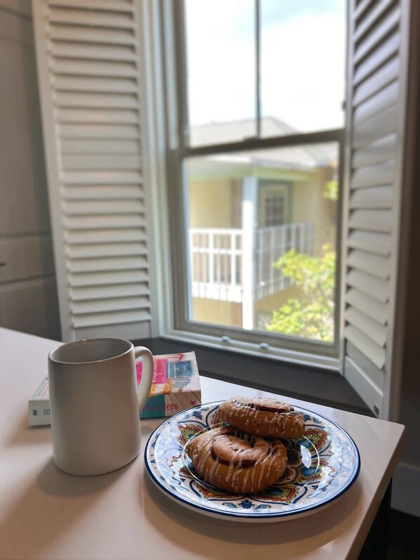 A table with a plate of pastries and a mug, near a window with blinds.