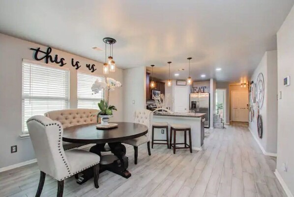 A dining area with a round table, white upholstered chairs, and pendant lighting.
