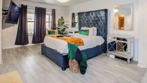 Un dormitorio con cama, mesita de noche, espejo y ventana con cortinas.