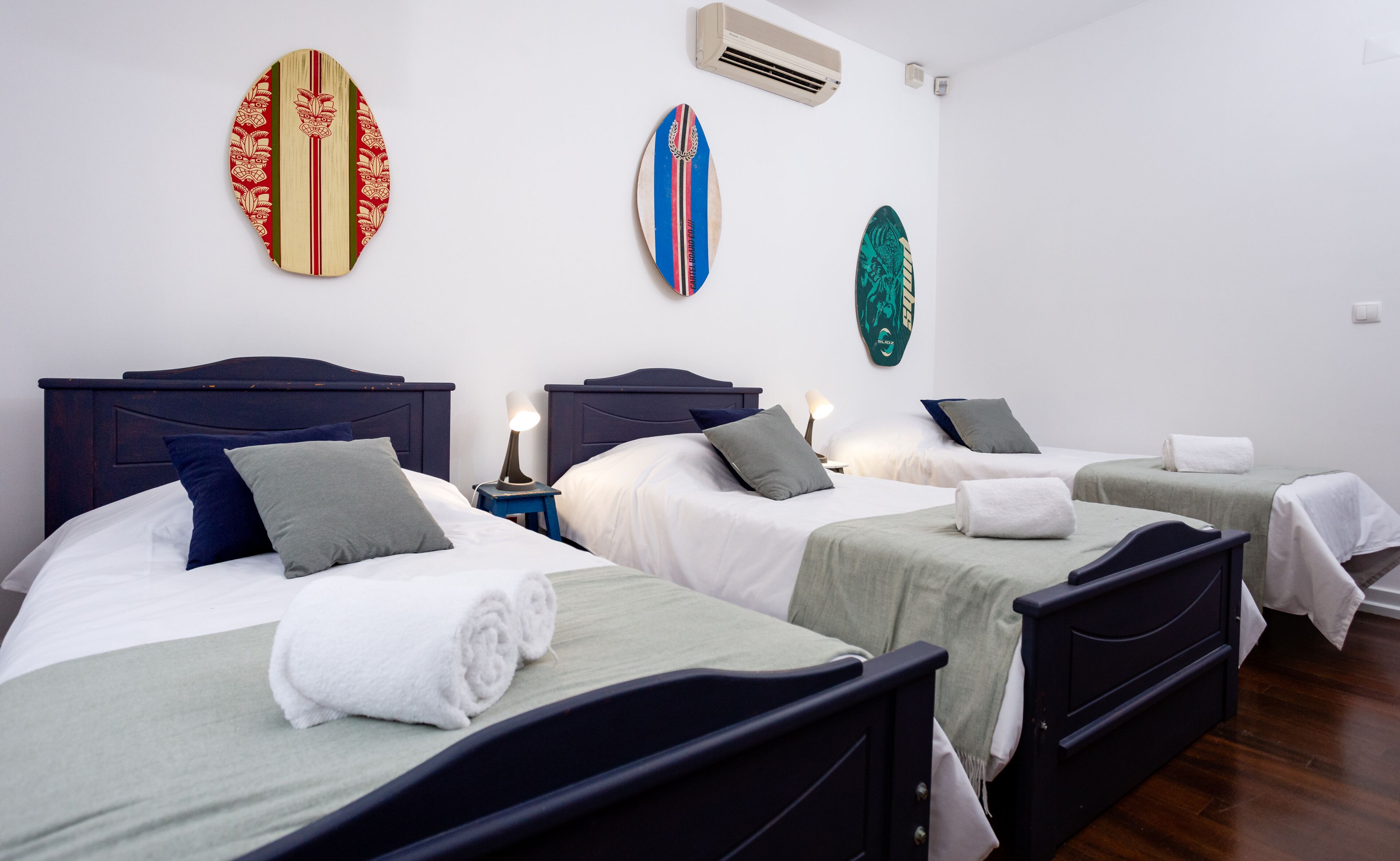 Camera d'hotel con tre letti, ciascuno con una decorazione a forma di tavola da surf a motivi diversi sulla parete.