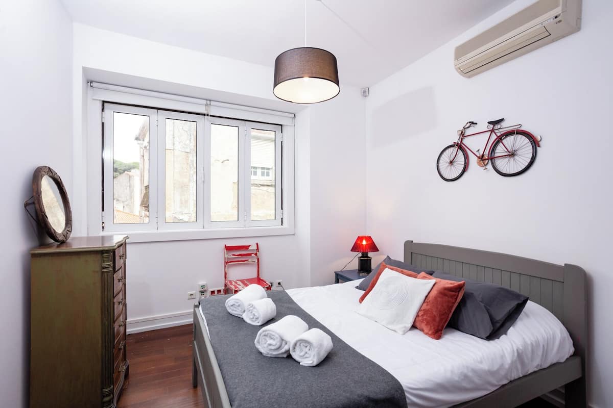A bedroom with a bed, a dresser, a window, a bicycle on the wall, and a lamp.