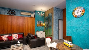 A living room with a black leather sofa, a white chair, a wooden coffee table, and a small round table with a toy bus. - Kais Do Sol - Hostel (Seixal)