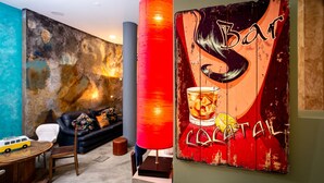 A room with a large abstract painting, a red cylindrical lamp, a black leather sofa, and a small wooden table with a toy car. - Kais Do Sol - Hostel (Seixal)