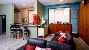 A living room with a sofa, two chairs, a coffee table, a bar area with stools, a mirror, and a window with blinds. - Kais Do Sol - Hostel (Seixal)