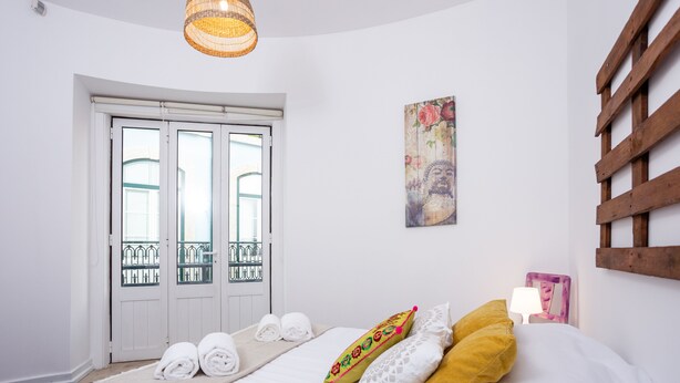 A bedroom with a bed, a window, a door, and a wall-mounted light fixture. - Kais Do Sol - Hostel (Seixal)