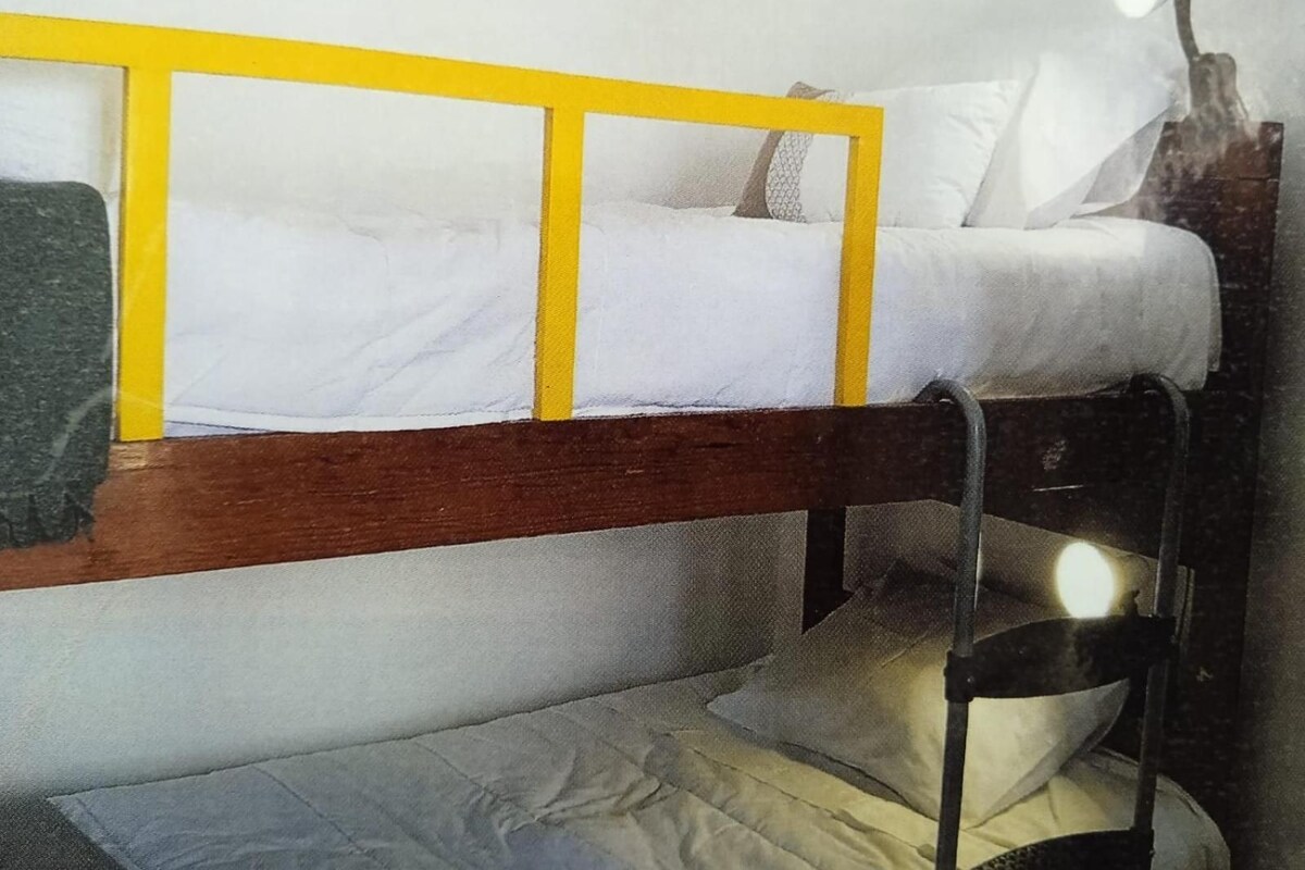 A bunk bed with a yellow frame, a bedside lamp, and a pillow.