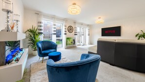 Un salon moderne avec un fauteuil bleu, un canapé noir, un aquarium et un logo Netflix sur le mur.