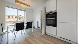Une cuisine moderne avec des meubles blancs, un four encastré et un coin repas comprenant une table et des chaises.