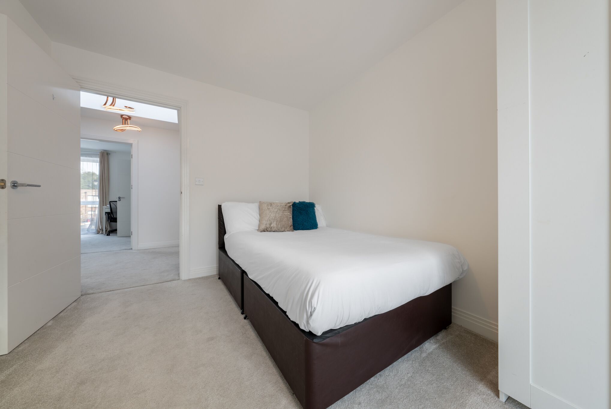 A bedroom with a single bed, a door leading to another room, and a ceiling light fixture.