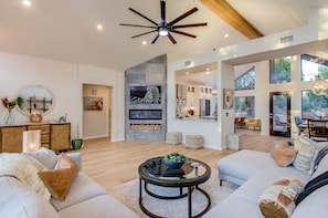 Amplia sala de estar con un ventilador de techo moderno, una chimenea y un gran ventanal con vistas al exterior.