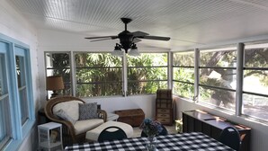 Une véranda avec une table à carreaux, des meubles en osier et un ventilateur de plafond.