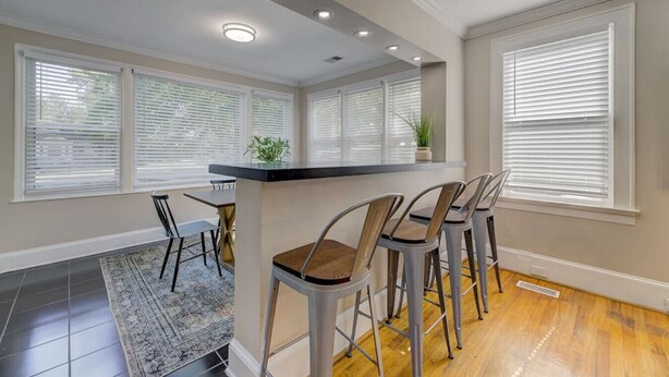 A modern kitchen with a bar area, large windows, and a dining table with chairs.