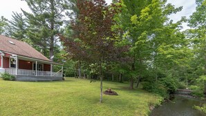 Une maison avec un porche, un petit étang et des arbres tout autour.