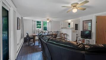 A modern living room with a black leather sofa, dining table, chairs, and a ceiling fan.