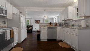 Une cuisine avec des meubles blancs, un four à micro-ondes, un réfrigérateur et un lave-vaisselle. Une fenêtre offre une vue sur la verdure environnante.