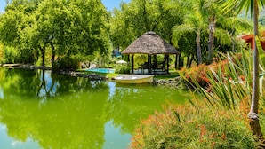A tranquil garden with a pond, a boat, and a thatched-roof gazebo.