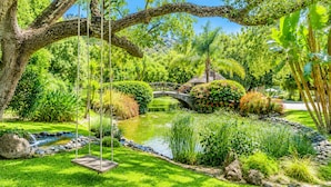 A garden with a swing, a pond, and a stone bridge.