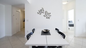 Zona pranzo con tavolo bianco, sedie nere e un elemento decorativo a parete.