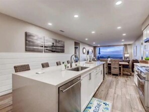 A modern kitchen with a central island, a dining area with a view, and a large window. - Gorgeous Oceanside Sunsets on The Strand-Watch Waves and Dolphins (Oceanside)