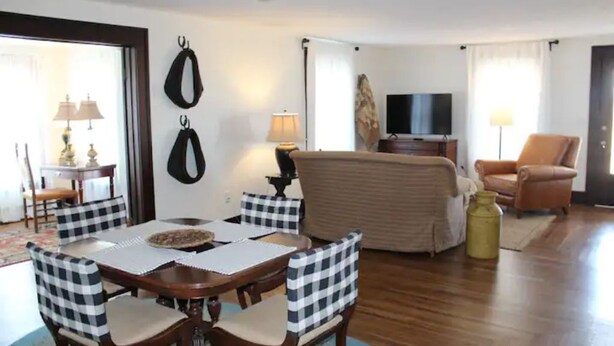A living room with a dining table, checkered chairs, a sofa, a TV, and a lamp. - Cozy 1920s Farmhouse in the Ozark hills (Green Forest)