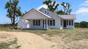 A single-story white house with a front porch, a small attached garage, and a fenced yard. - Cozy 1920s Farmhouse in the Ozark hills (Green Forest)