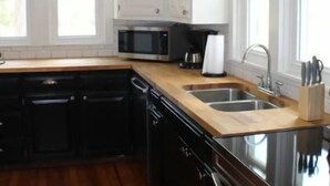 A modern kitchen with white cabinets, a stainless steel sink, a microwave, and a large island with a built-in oven. - Cozy 1920s Farmhouse in the Ozark hills (Green Forest)