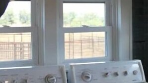 A laundry room with two washing machines and a large cow skull decoration above the windows. - Cozy 1920s Farmhouse in the Ozark hills (Green Forest)