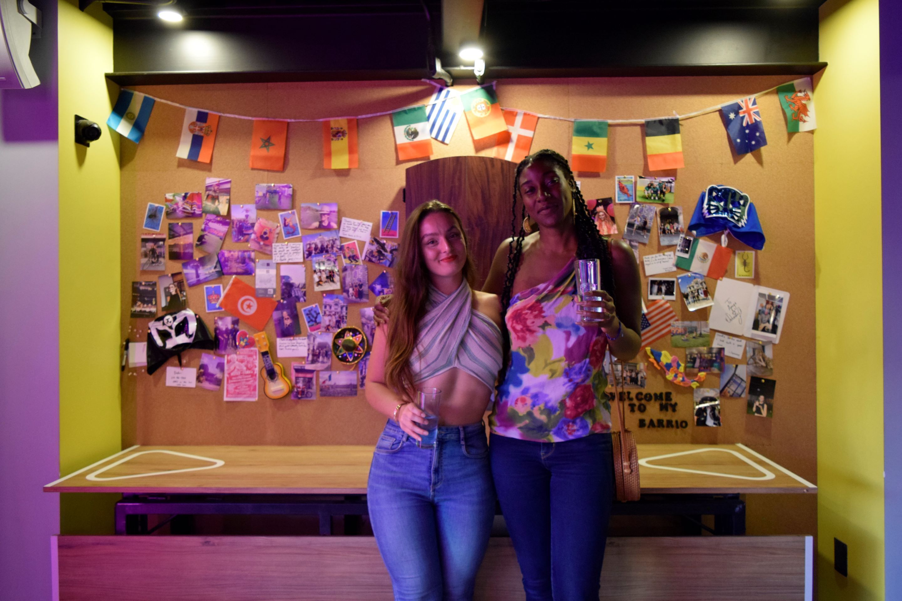 Two people standing in front of a wall decorated with flags and photos.