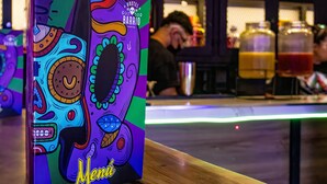 Un atril de menú colorido con un diseño festivo, sobre una mesa de madera en un bar.