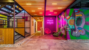 Un pasillo vibrante con una escalera, un letrero de neón que dice "MEXICO mística" y murales coloridos.