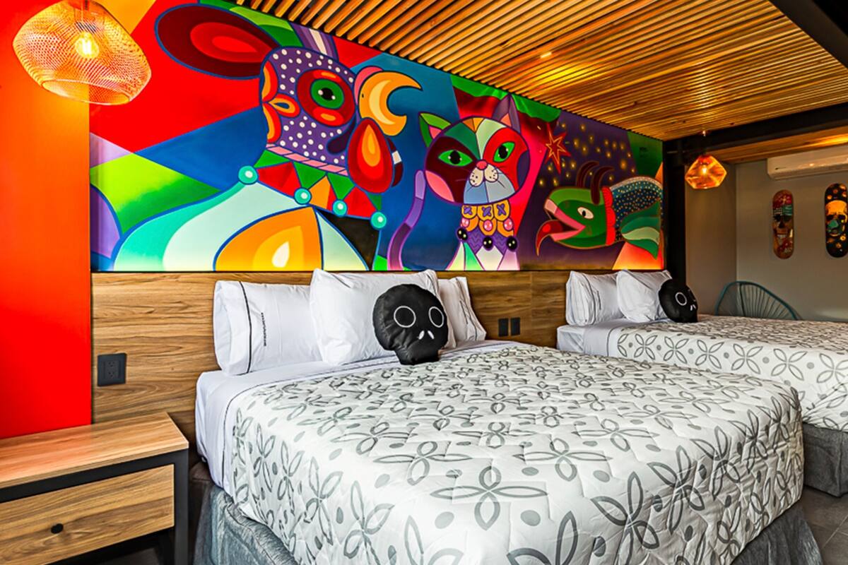 A hotel room with two beds, a colorful abstract mural on the wall, and a modern wooden ceiling.