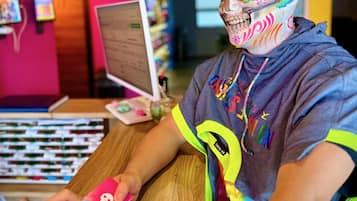A person seated at a wooden table with a computer monitor, surrounded by colorful decorations and a vibrant pink wall.