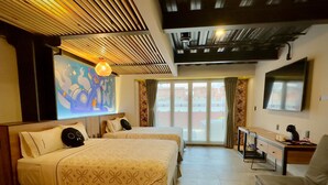 Habitación de hotel con dos camas, un escritorio, televisor y balcón con vistas.