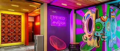 Un lobby de hotel vibrante con un mural colorido, un letrero de neón que dice "Mexico Mágica" y una silla moderna.