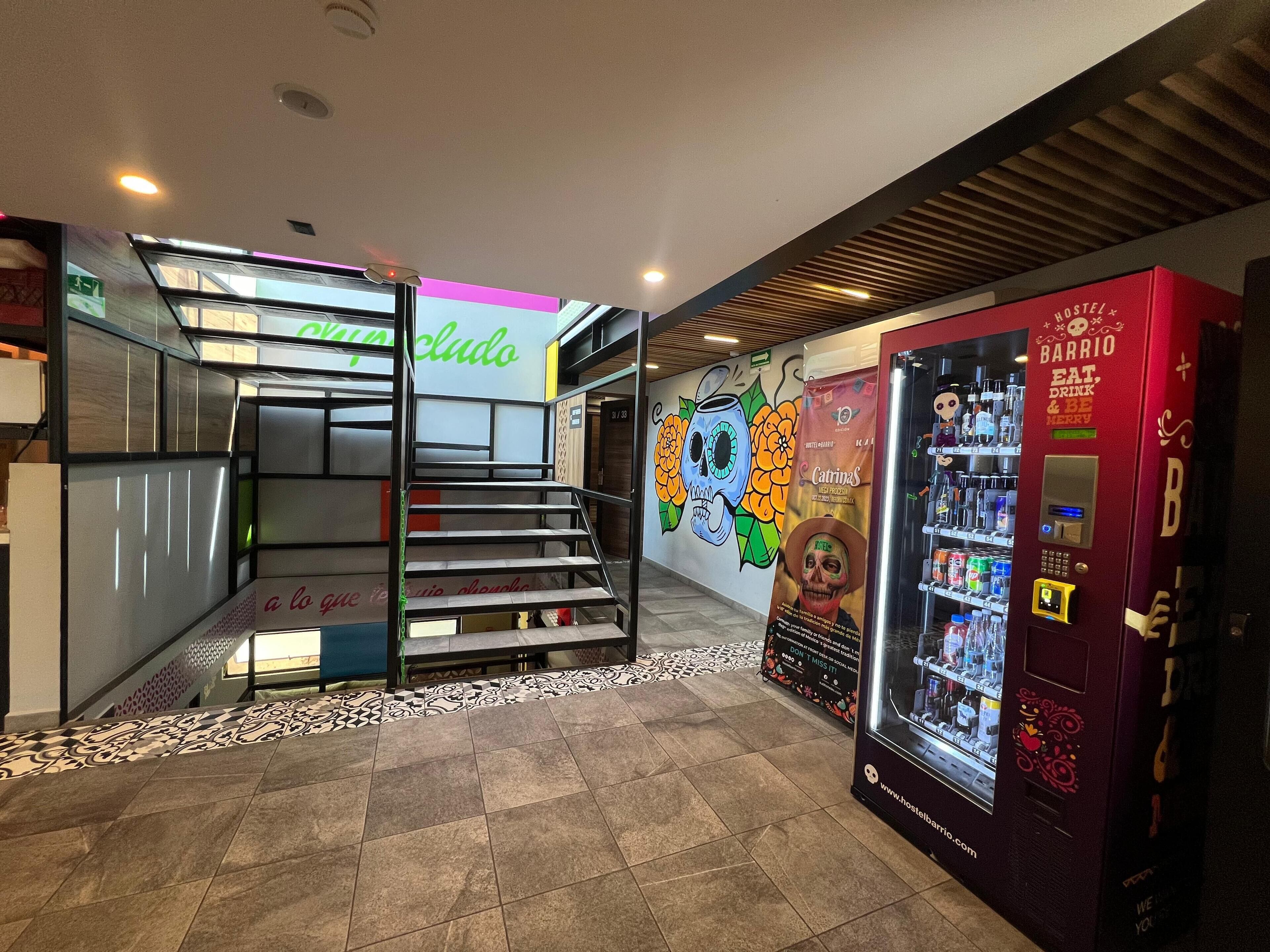 A hotel lobby with a staircase, a vending machine, and a mural.