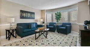 Una sala de estar con un sofá azul, dos sillones, una mesa de centro y un tapete estampado.
