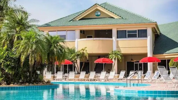 Un hotel con piscina, sombrillas rojas y palmeras.