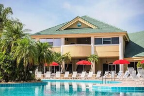 A hotel with a swimming pool, red umbrellas, and palm trees. - 2 Bedroom Luxury Resort - 1 Mile from Disney (Kissimmee)
