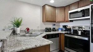 Una cocina con encimeras de granito, gabinetes de madera, microondas, estufa, lavavajillas y pileta.