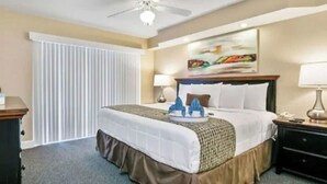 Habitación de hotel con cama, lámparas de noche, ventilador de techo, un cuadro en la pared y una ventana con persianas.