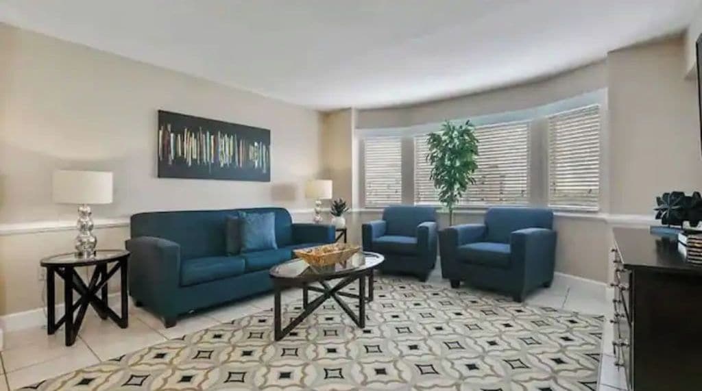 Un salon avec un canapé bleu, deux fauteuils, une table basse et un tapis à motifs.