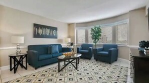 Una sala de estar con un sofá azul, dos sillones, una mesa de centro y un tapete estampado.