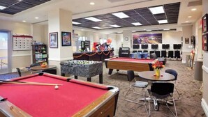 A pool area with multiple pool tables, a foosball table, and a bar area with a television screen. - Charming 1 BR Vegas Resort | Pools & much more. (Kissimmee)
