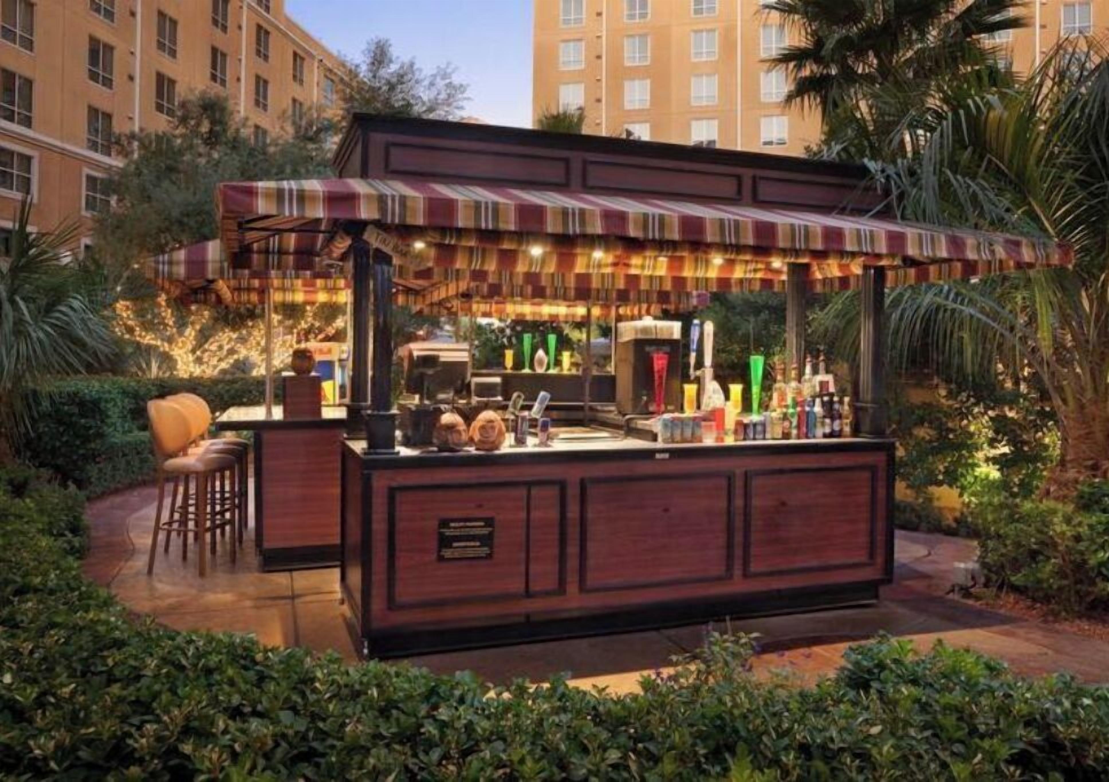 Un espace bar doté d’un auvent rayé, de tabourets de bar et d’une variété de bouteilles.