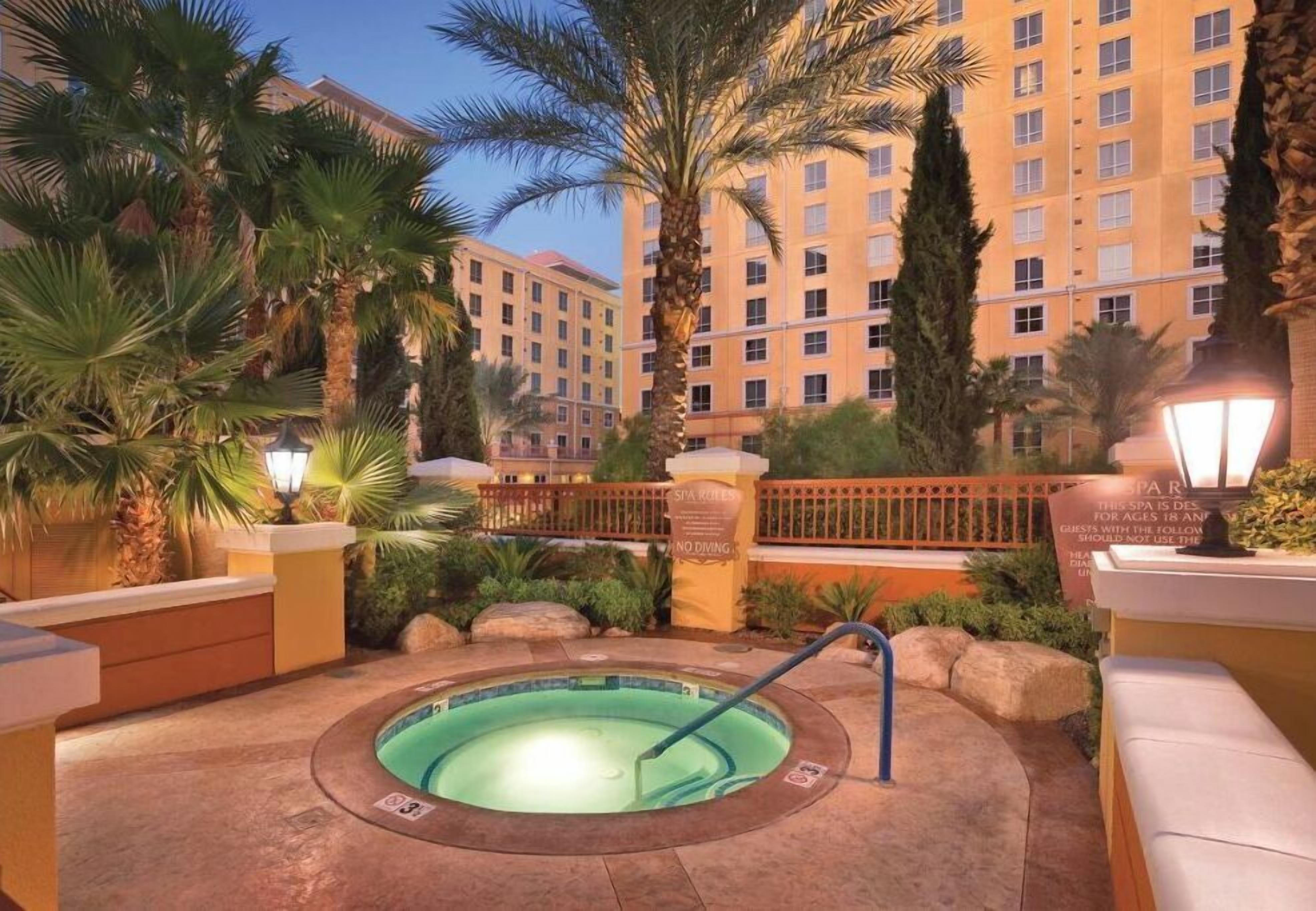 A hot tub surrounded by palm trees and a hotel building in the background.