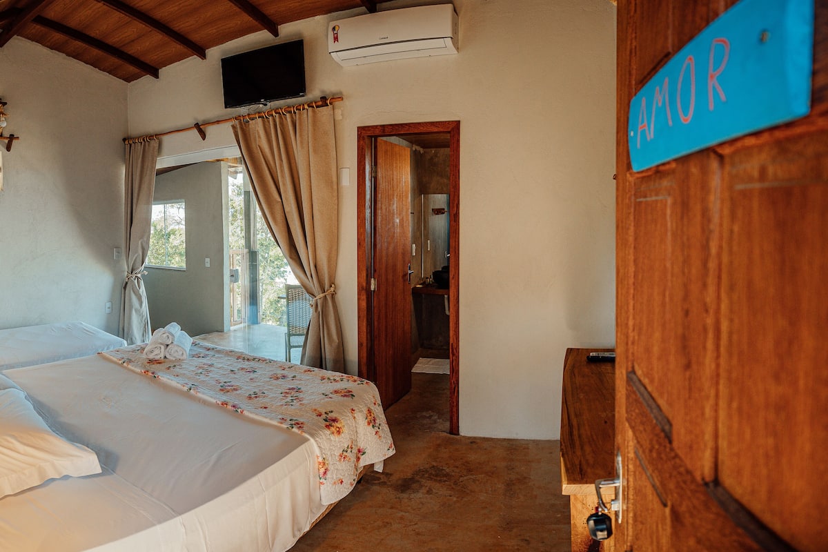 A bedroom with a bed, a wooden desk, a TV, and a sign reading "AMOR".